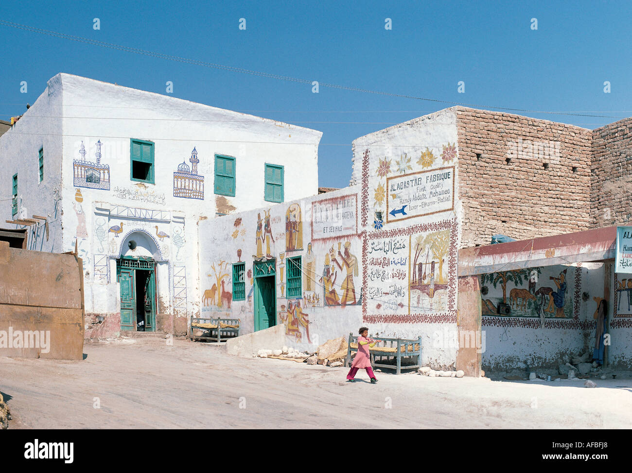 A girl walking past the Alabaster Factory in a village of painted Arab houses near the Valley of the Kings Egypt Stock Photo