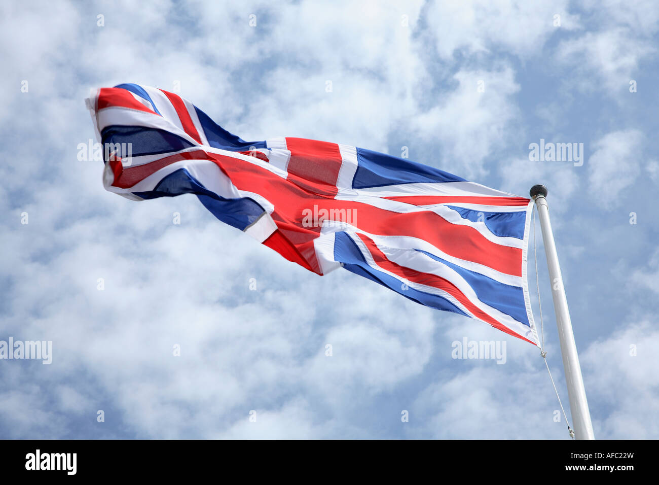 The Union Jack flag blowing in the wind with a blue sky and clouds in the background Stock Photo