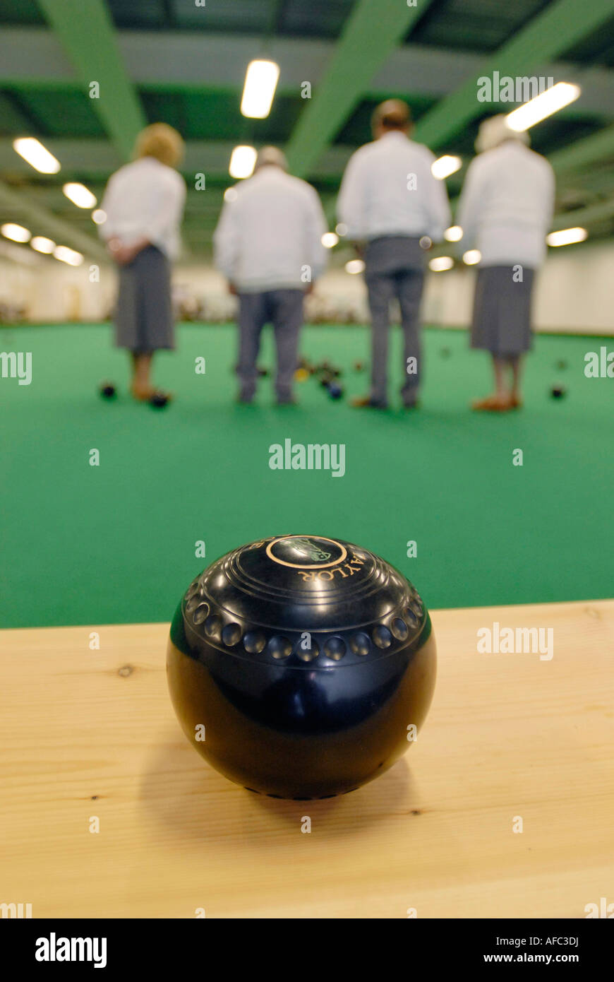 Bowling ball with bowlers competing at an indoor bowls green. Stock Photo