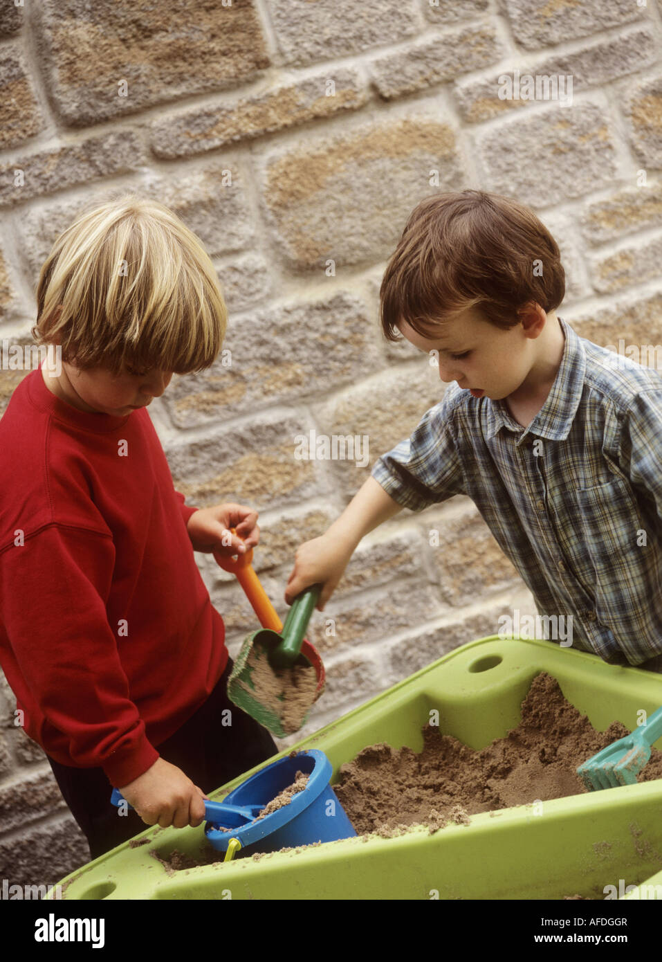 Young boys playing with a plastic spade and containers in a sand tray ...
