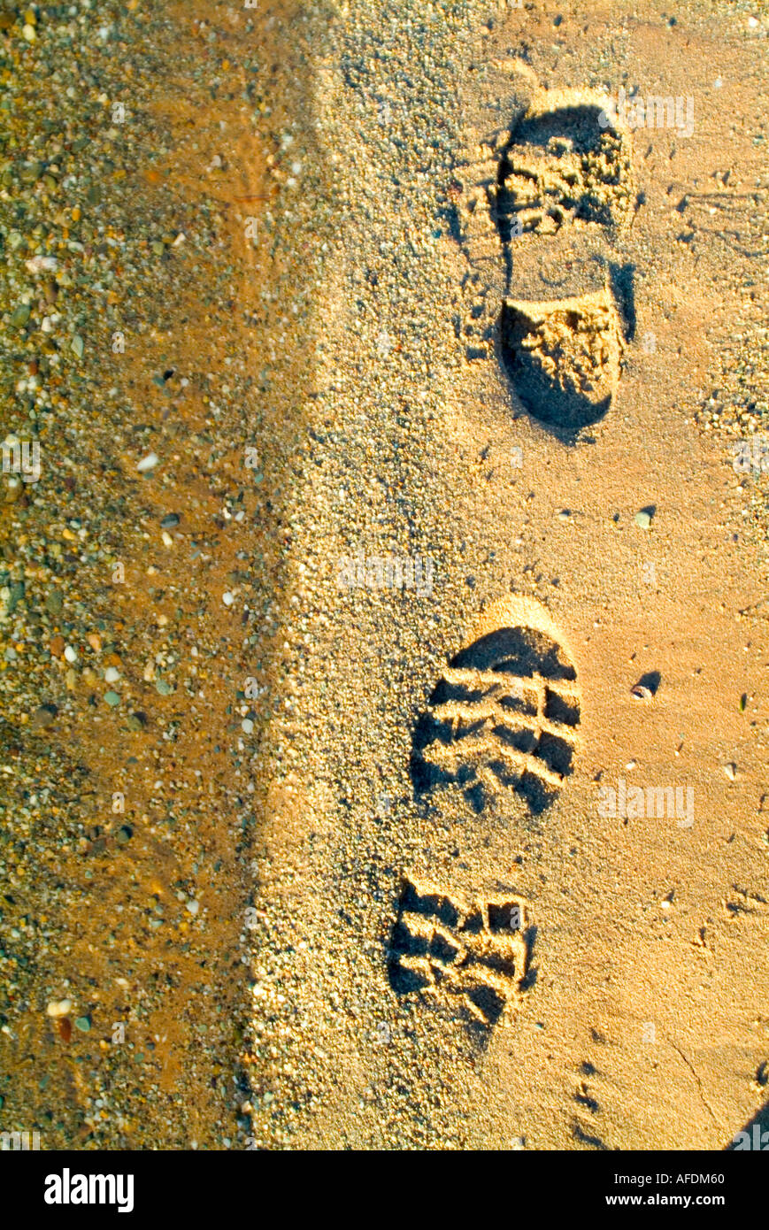 boot prints in the sand beside the waters edge Stock Photo