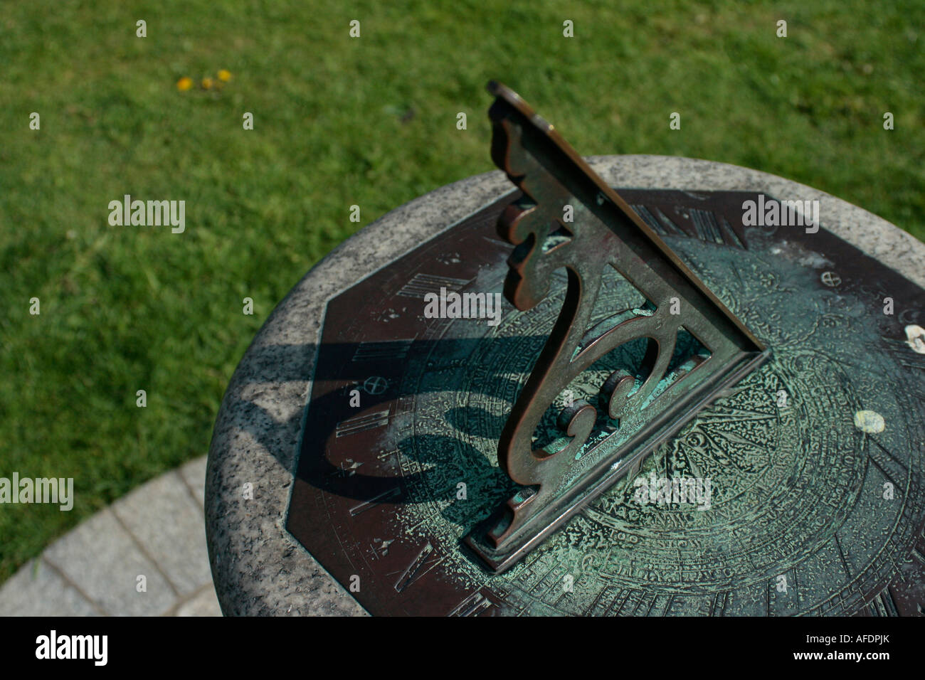 Sundial, copper metal on granite stand surrounded by green grass lawn Stock Photo