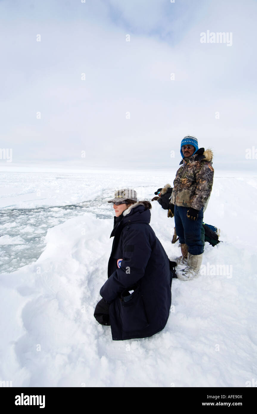 Armed Inuit guard protects French Canadian journalist Sarah champagne from possible polar bear attack at the floe edge of the ic Stock Photo