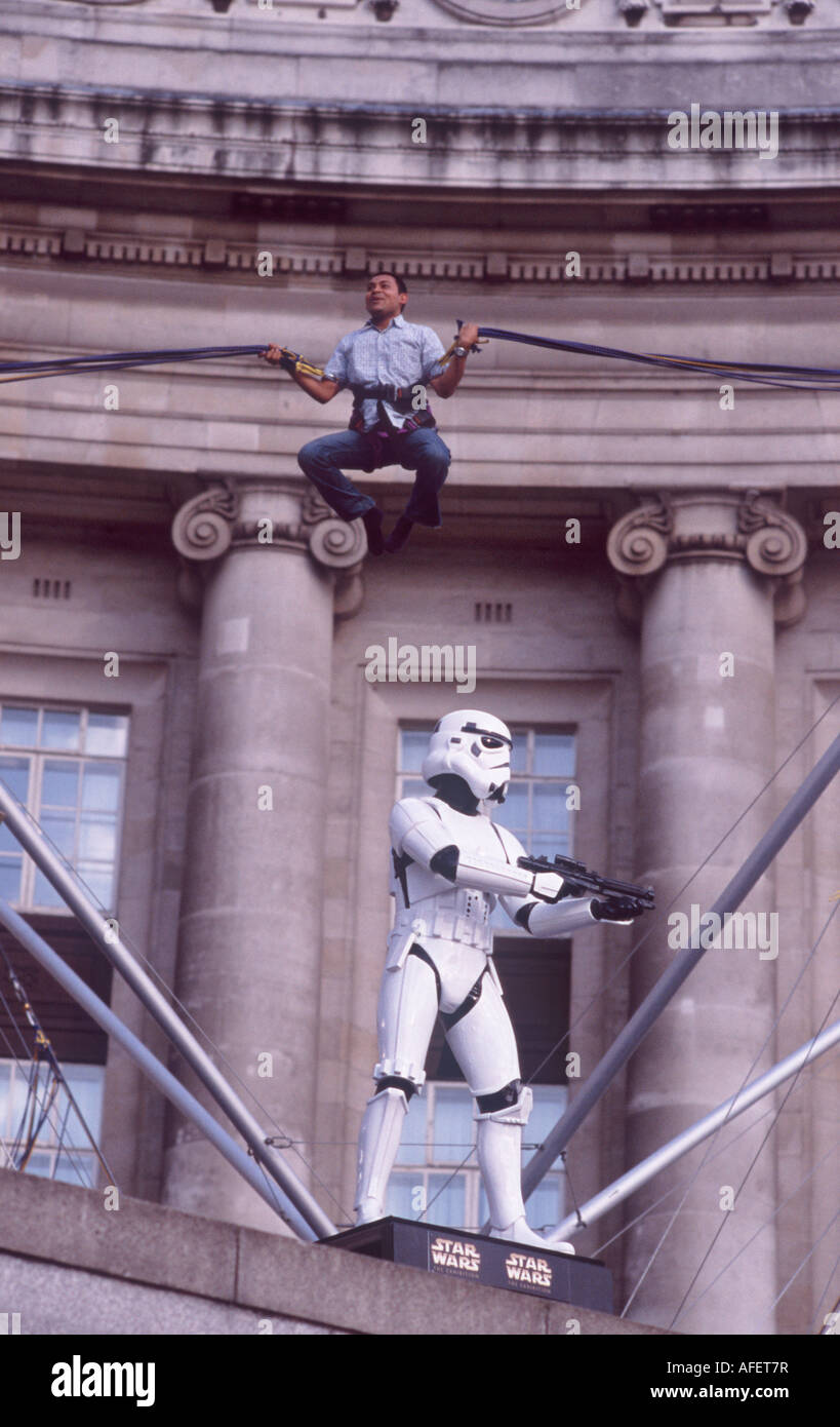 Smiling jumping man on bungy cord flying over head of a Star Wars Storm Trooper before London County Hall, London Stock Photo