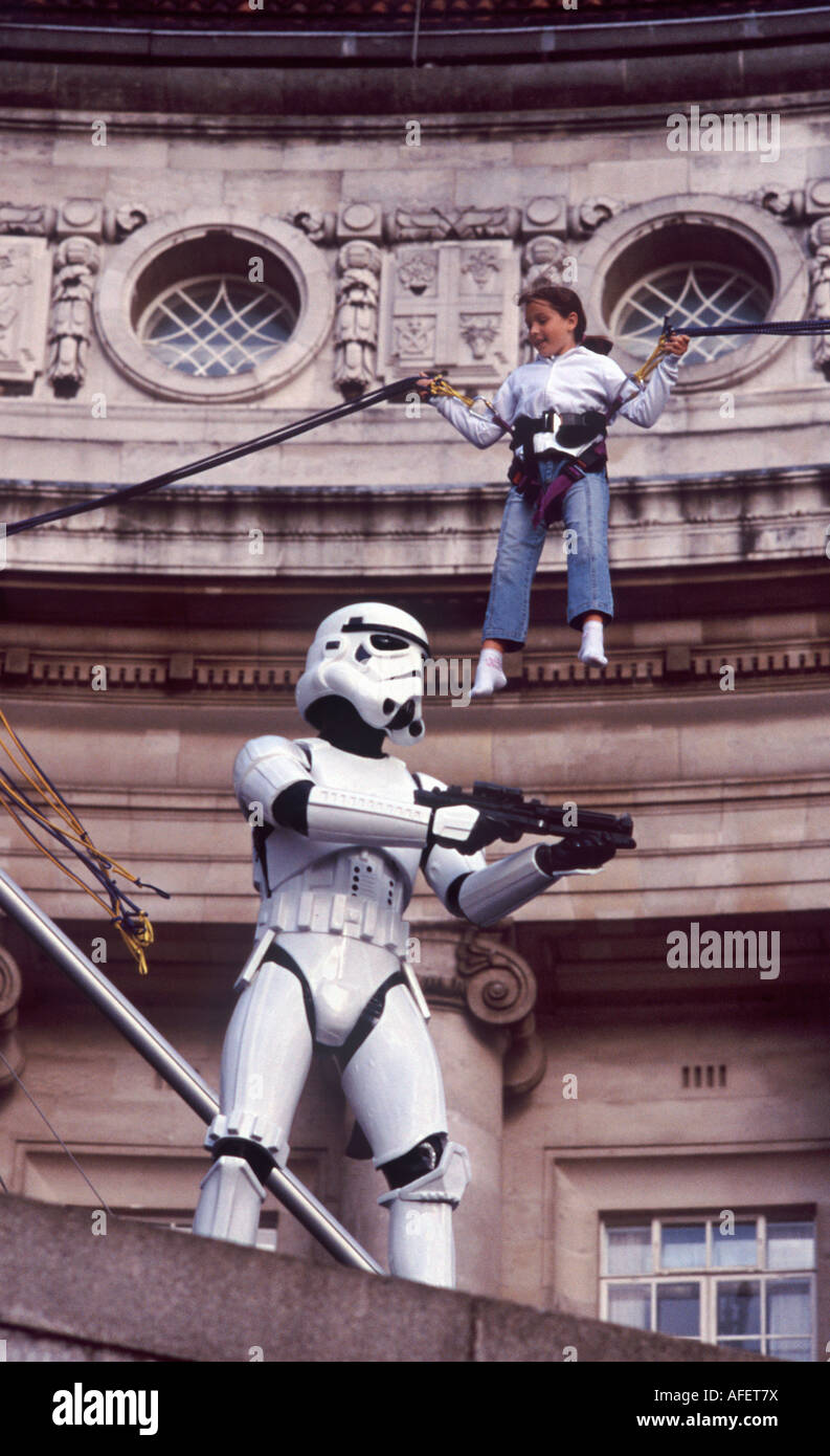 Little girl jumping on bungy cord looking down on a Star Wars Storm Trooper before London County Hall, South Bank, London Stock Photo