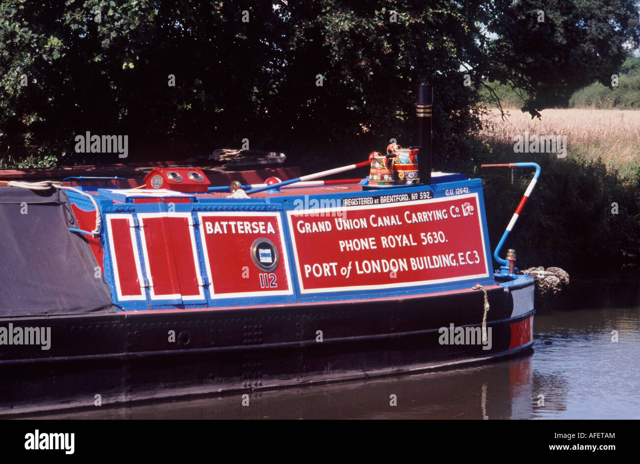 Brightly painted traditional working narrowboat (Grand Union Canal Carrying Co) with striped tiller and canalware, Staffordshire Stock Photo