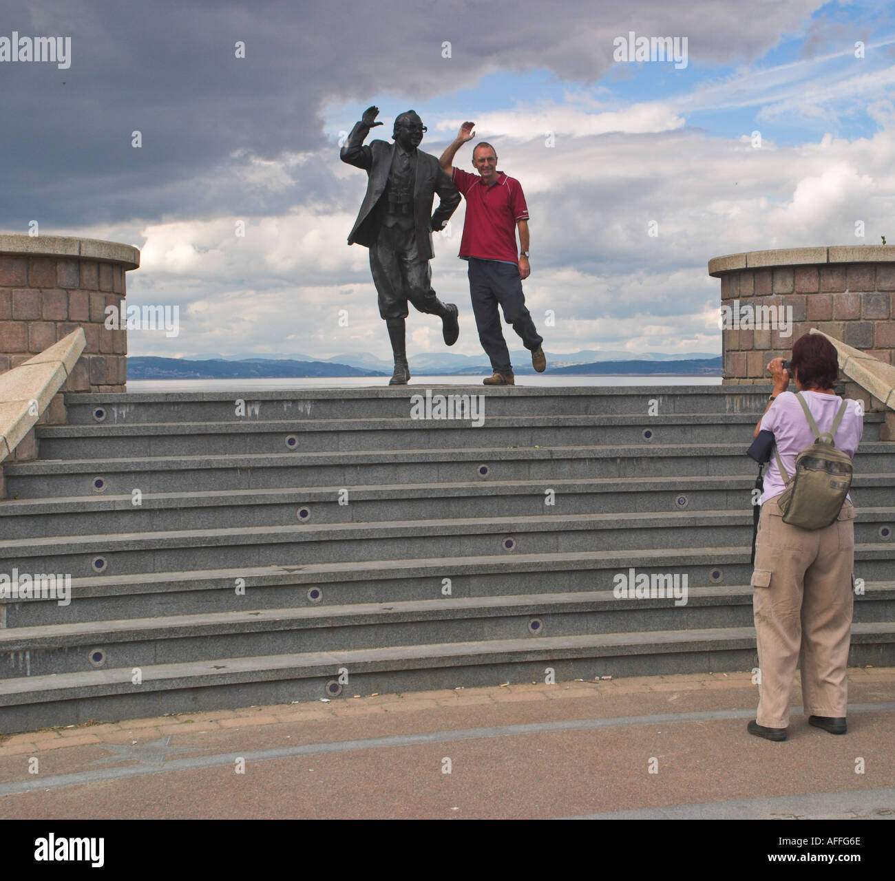 A tourist has his photograph taken with statue of Eric Morecambe. Morecambe, Lancashire, United Kingdom Stock Photo