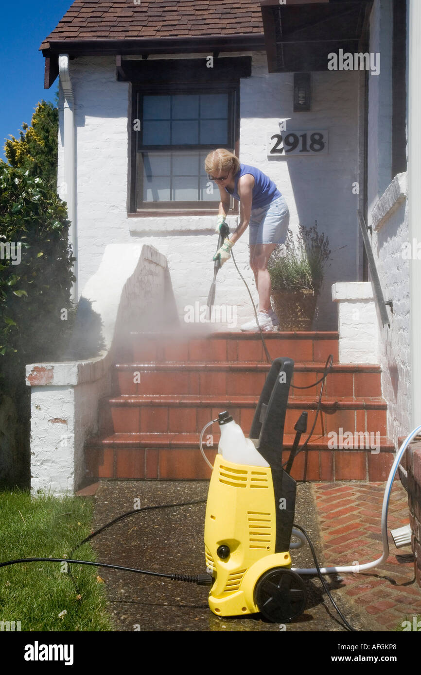Woman using pressure washer to clean front porch of her home Seattle