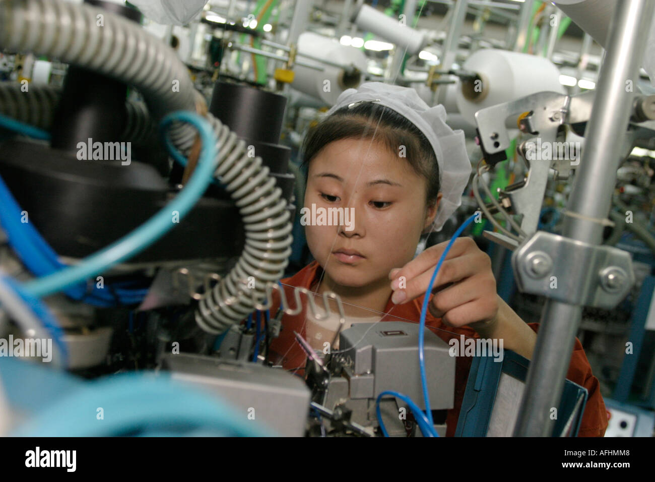 China. Woman machinist checks thread on the production line of the Langsha Sock and Stocking Corporation Stock Photo