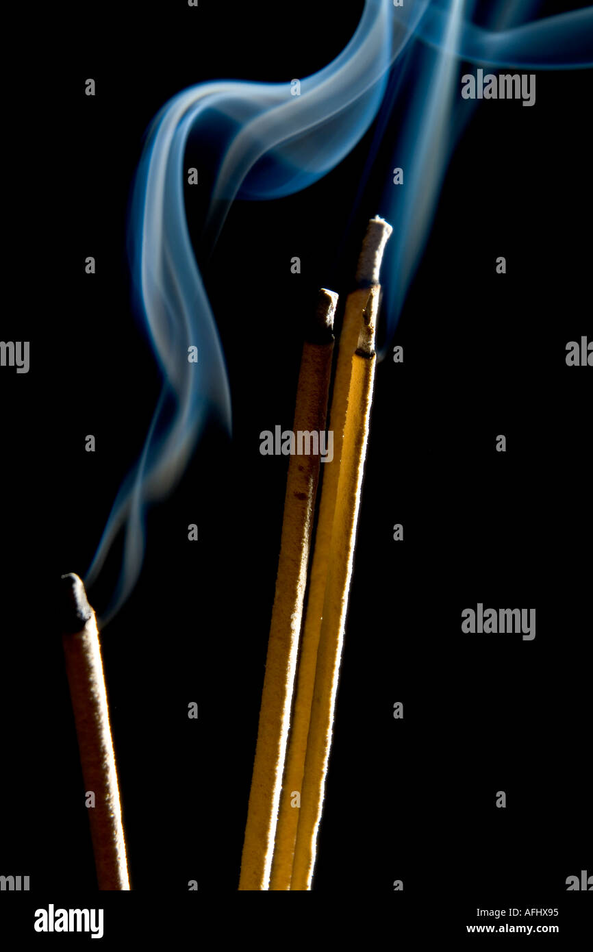 Sticks of incense burning against black background with blue smoke