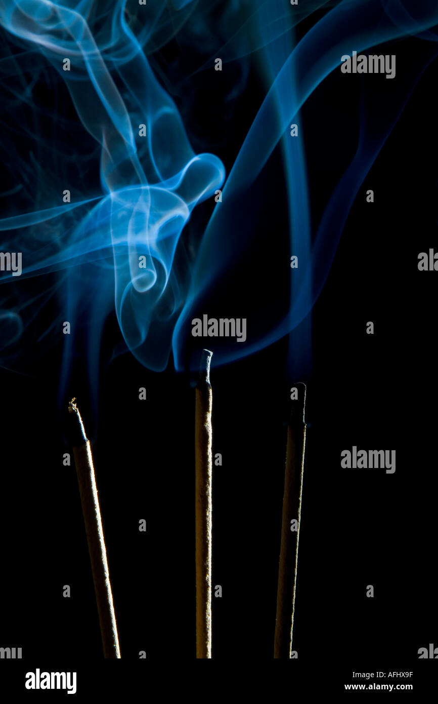 Sticks of incense burning against black background with blue smoke
