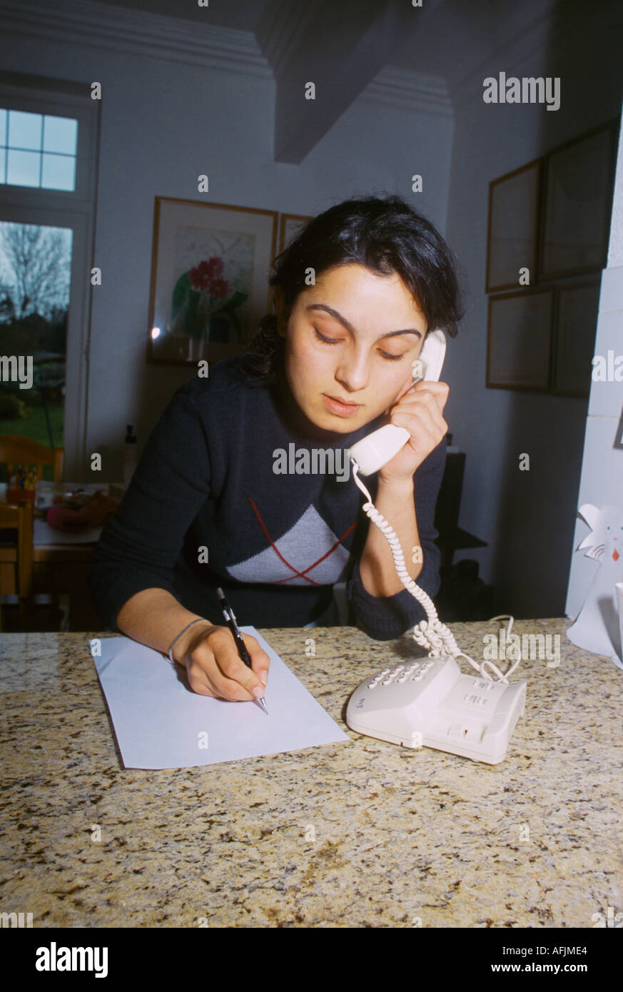 Young Woman Answering Phone At Home Taking Message Stock Photo