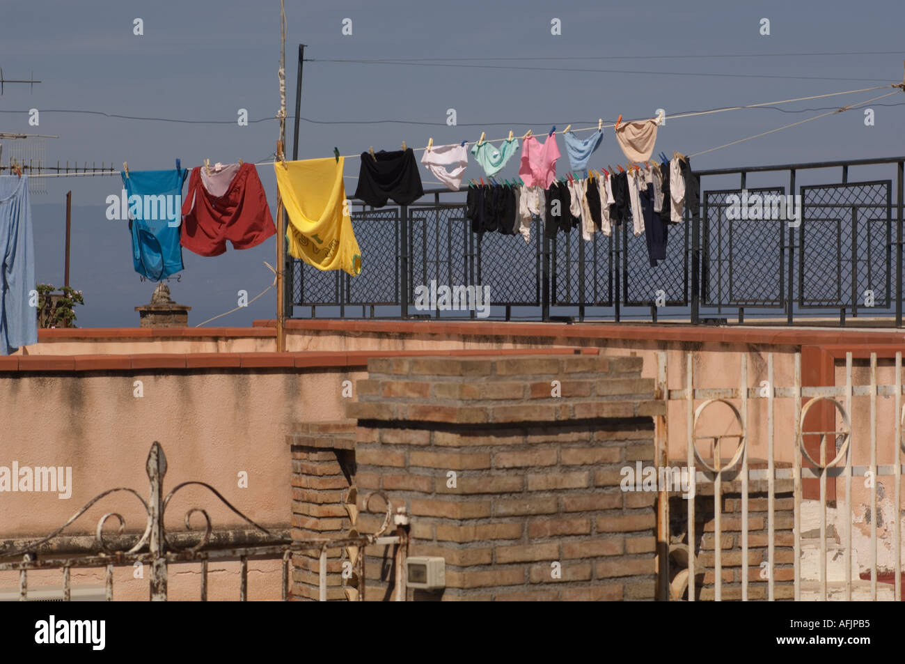 colorful laundry hanging on a clothes line over some stucco and brick walls and wrought iron fences with blue sky and sea behind Stock Photo