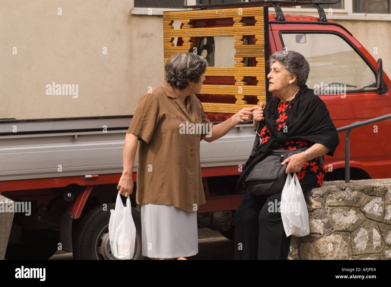 Two elderly Sicilian women arguing on the street with shopping bags in their hands Stock Photo