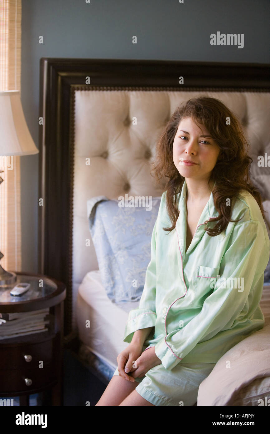 Young woman sitting on edge of bed Stock Photo - Alamy