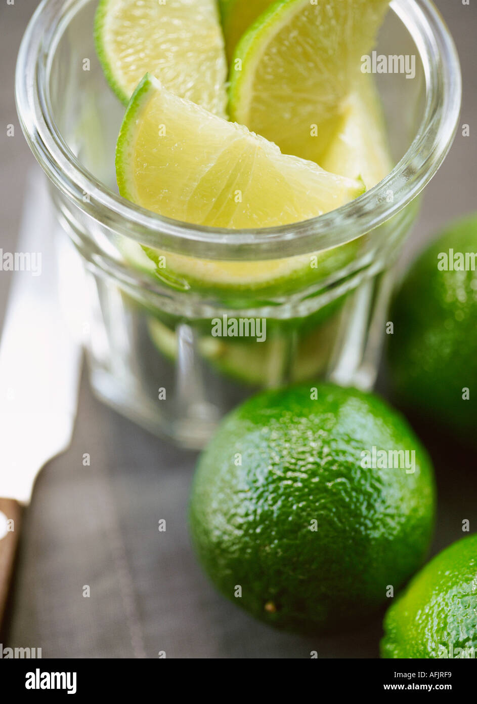 Sliced limes and whole limes in glass bowl with knife Stock Photo