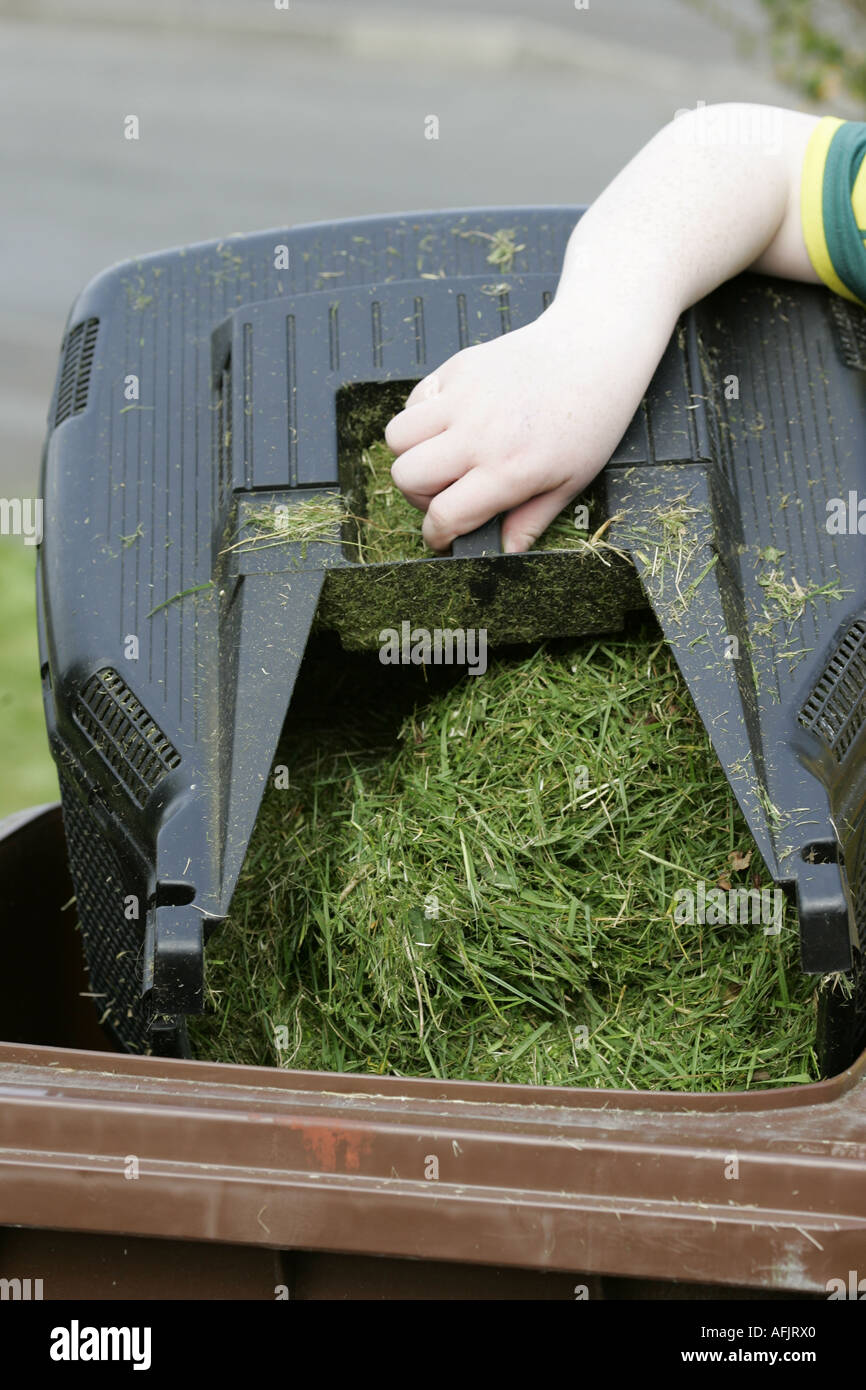 hand of young boy emptying lawnmower cut grass container into brown