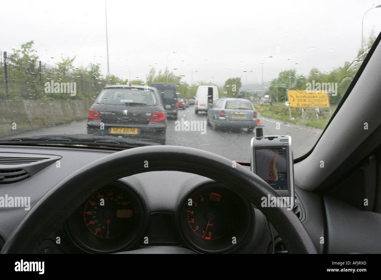 dashboard and steering wheel of car stuck in traffic on rainy day using PDA sat nav on westlink Stock Photo