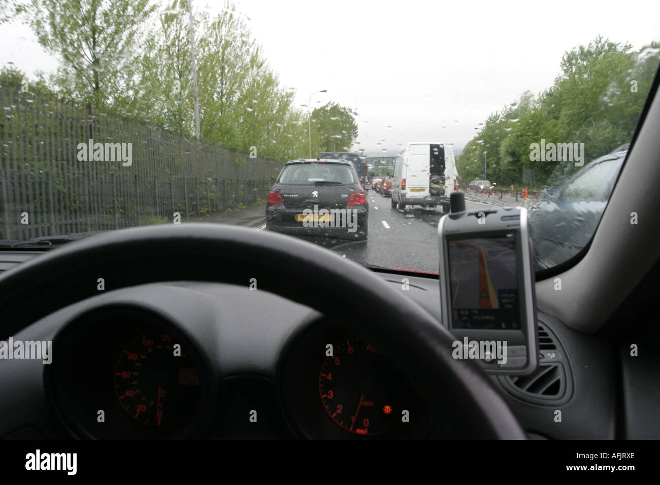 dashboard and steering wheel of car stuck in traffic on rainy day using