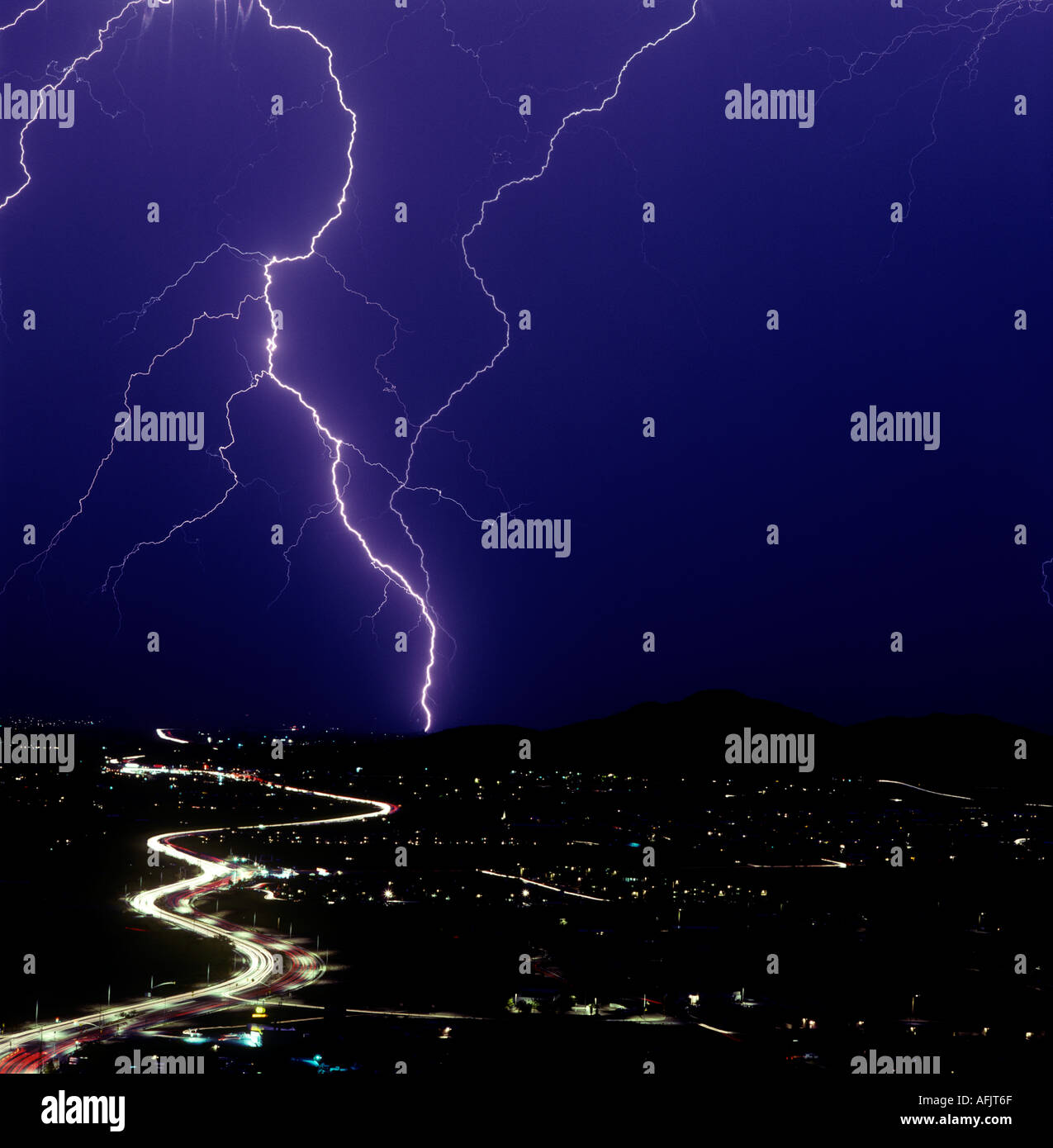 Lightning bolts strike down against the lights of the city and cars trailing down a nearby road during a monsoon in Tucson, AZ. Stock Photo