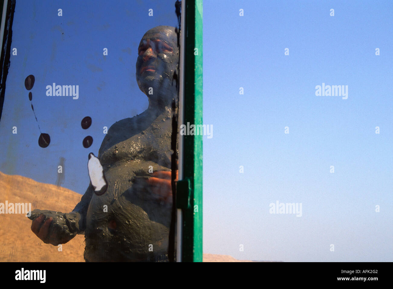A man smeared with natural black mud from the Dead Sea is reflected in