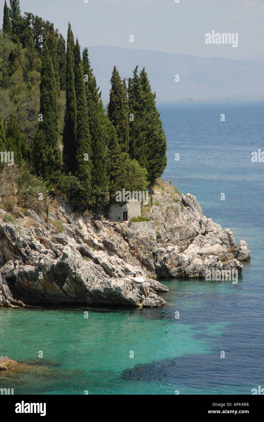 Small abandoned church on rocky outcrop with tall trees behind, near Nissaki beach, Corfu, Greece Stock Photo
