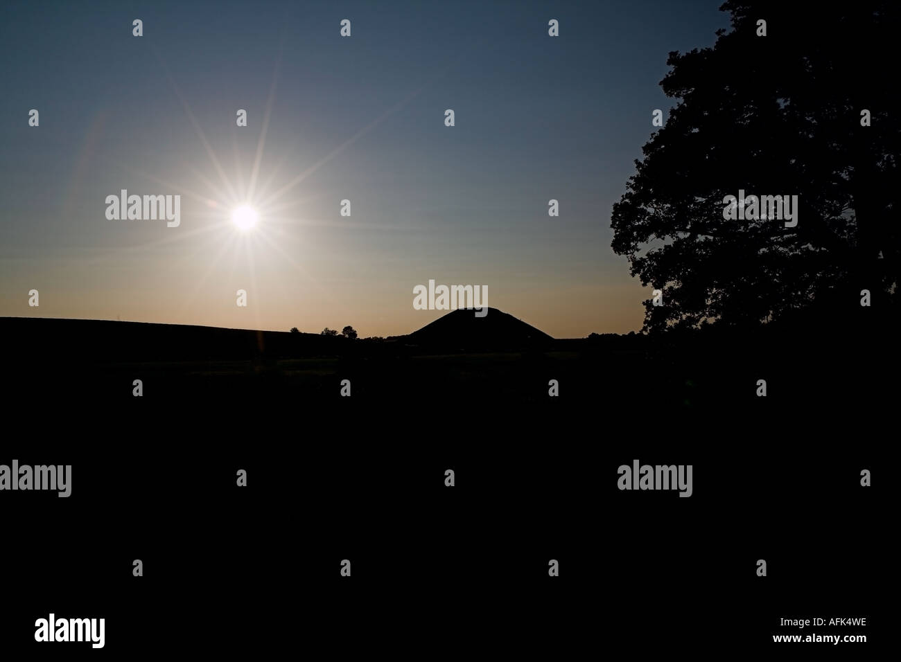 Silhouetted Silbury Hill Prehistoric Earth Mound against sunburst. Wiltshire, England, UK. Stock Photo