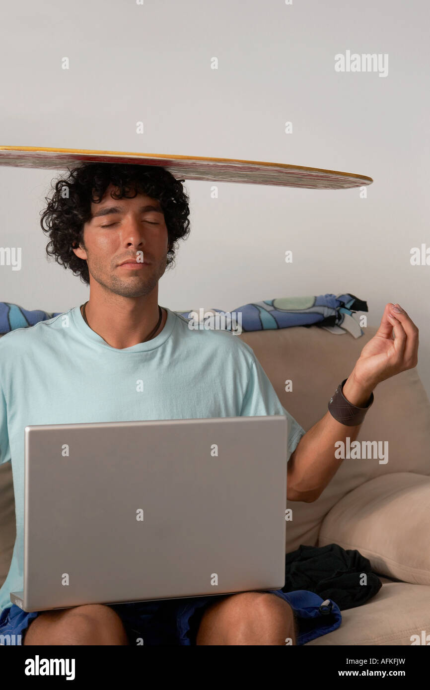 Young man sitting with a laptop in his lap and a body board  on his head Stock Photo