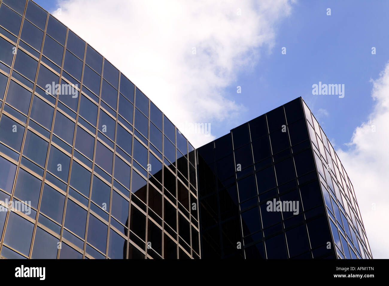 Modern smoked glass office building in shadow and light against a blue cloudy sky Stock Photo