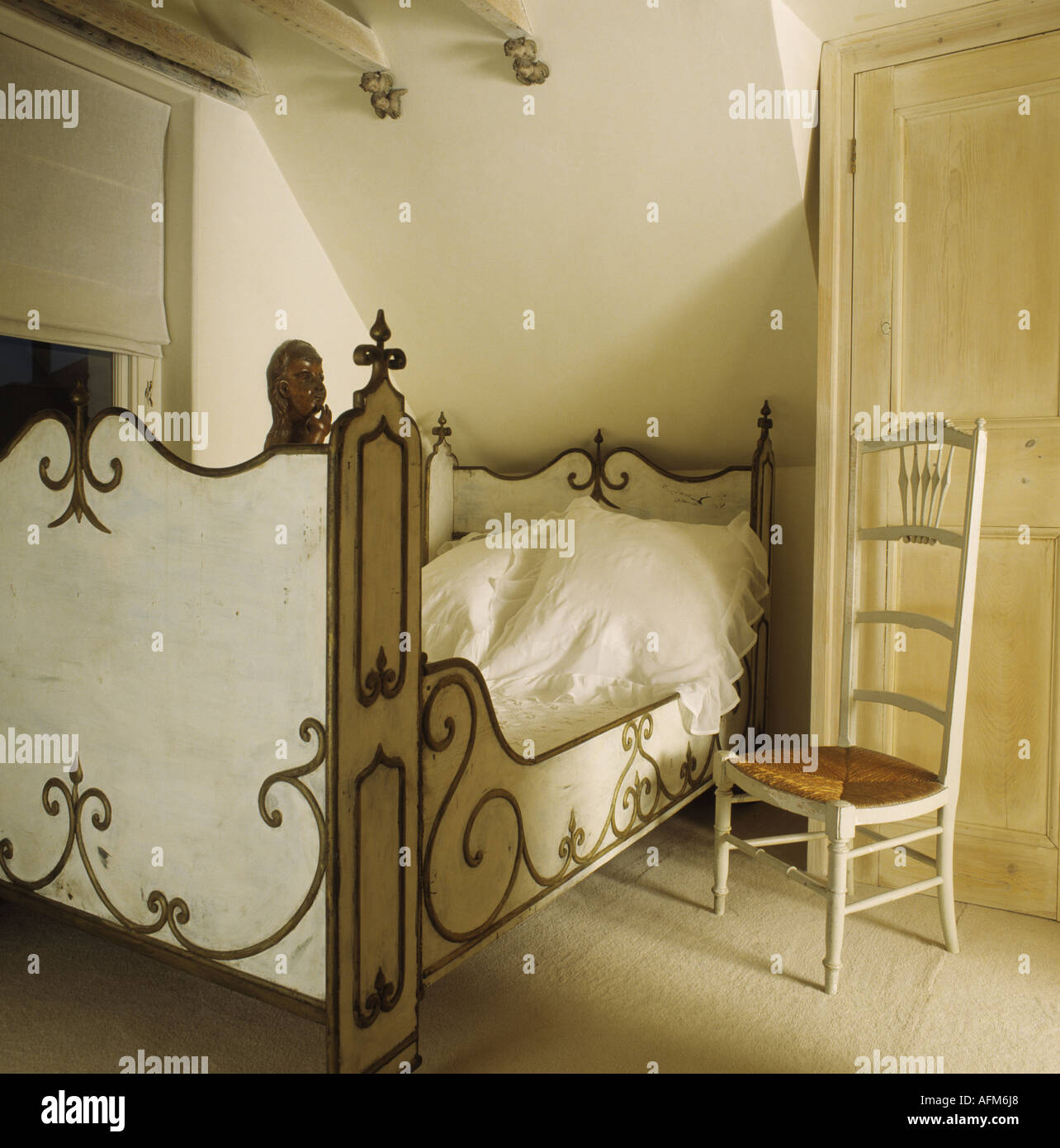 Antique rushseated cream chair beside bed with ornate footboard and