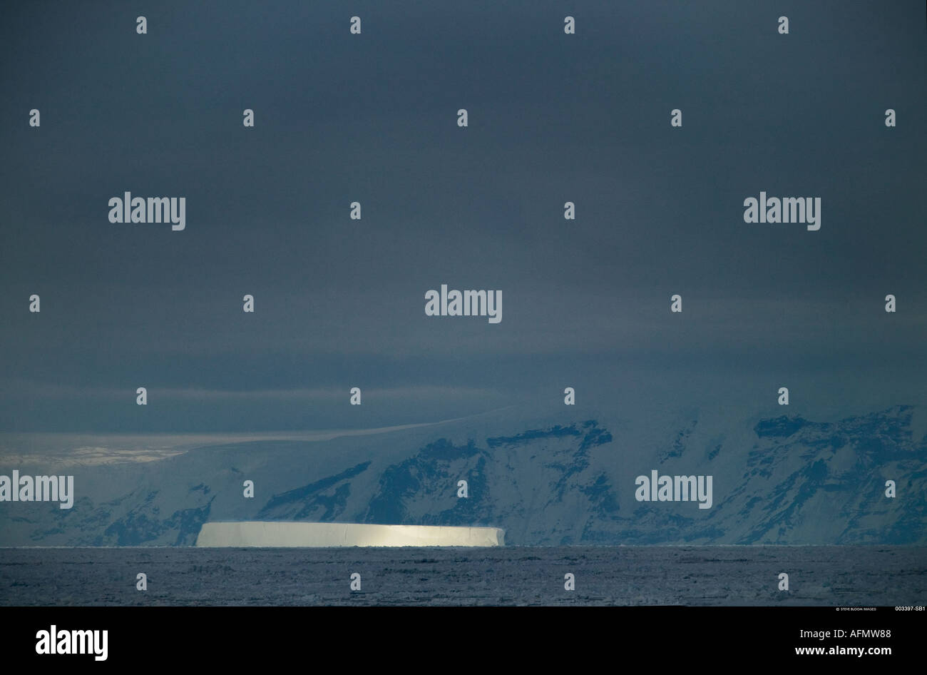 Stormy sky showing iceberg lit up by a shaft of sunlight Antarctica Stock Photo