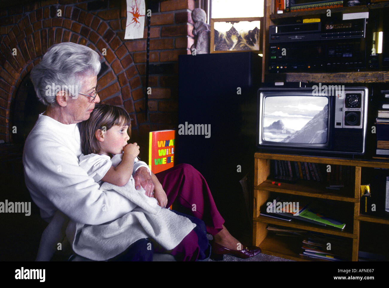 Grandmother with 3 year old granddaughter on her lap watches television Stock Photo