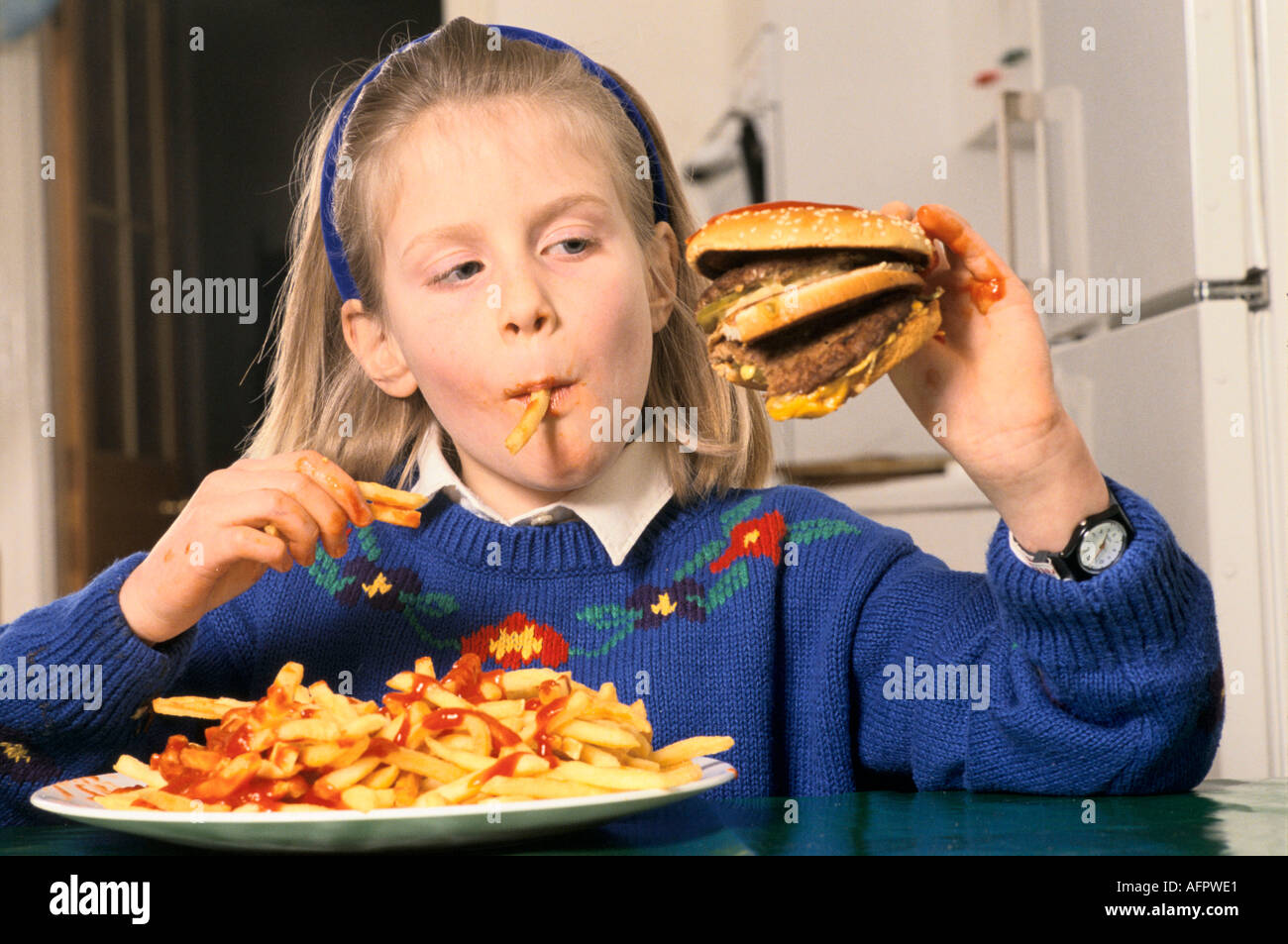 Junk food young schoolgirl teen eating a huge hamburger and chips drinking coke at home in after school London HOMER SYKES Stock Photo