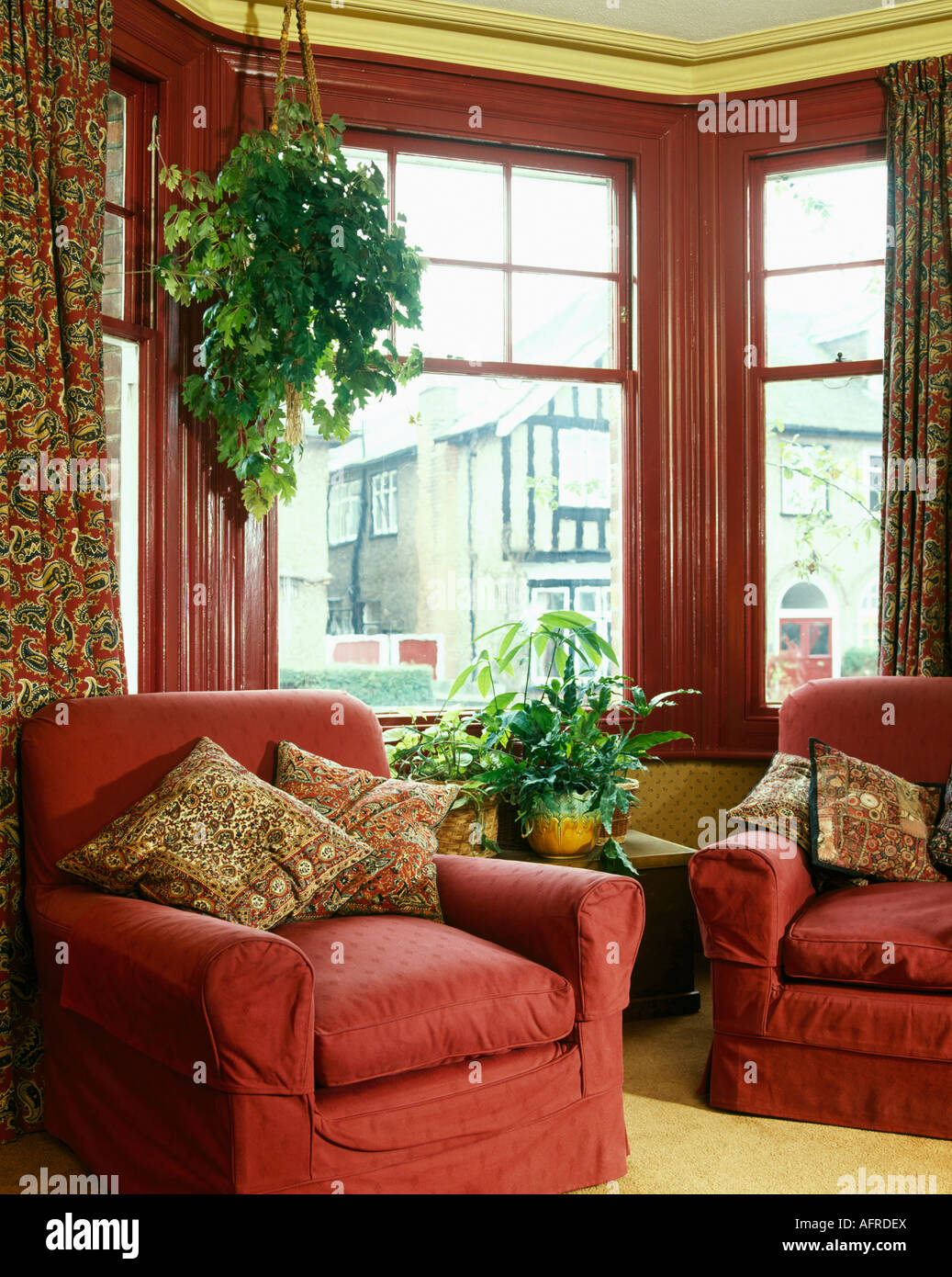 Comfortable Red Armchairs In Front Of Bay Window With Red Painted Frame In Nineties Living Room With Green Hanging Plants Stock Photo Alamy