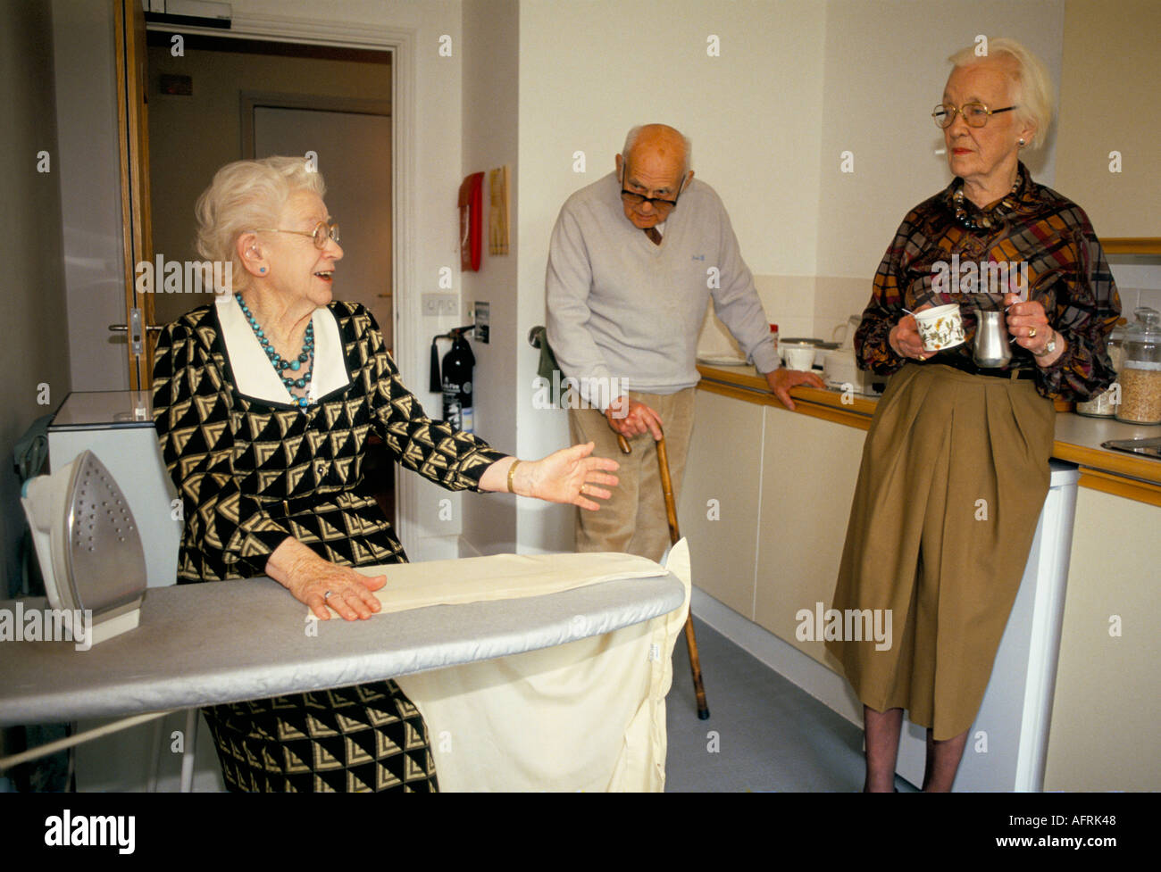 Residents in a residential care home. Doing domestic chores ironing and chatting to other residents. Cirencester Gloucestershire 1990s 1991 UK. Stock Photo