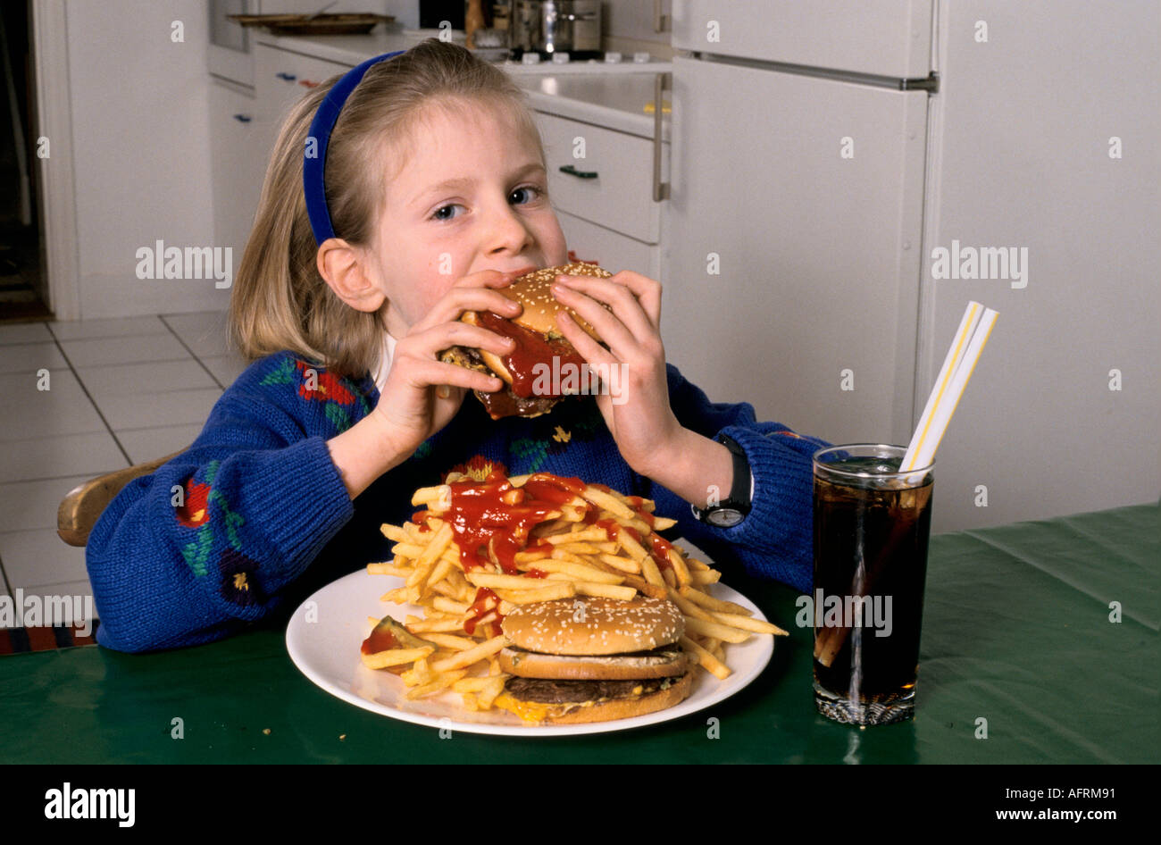 Junk food unhealthy overeating teen young schoolgirl eating a huge hamburger and chips drinking coke at home in after school London HOMER SYKES Stock Photo