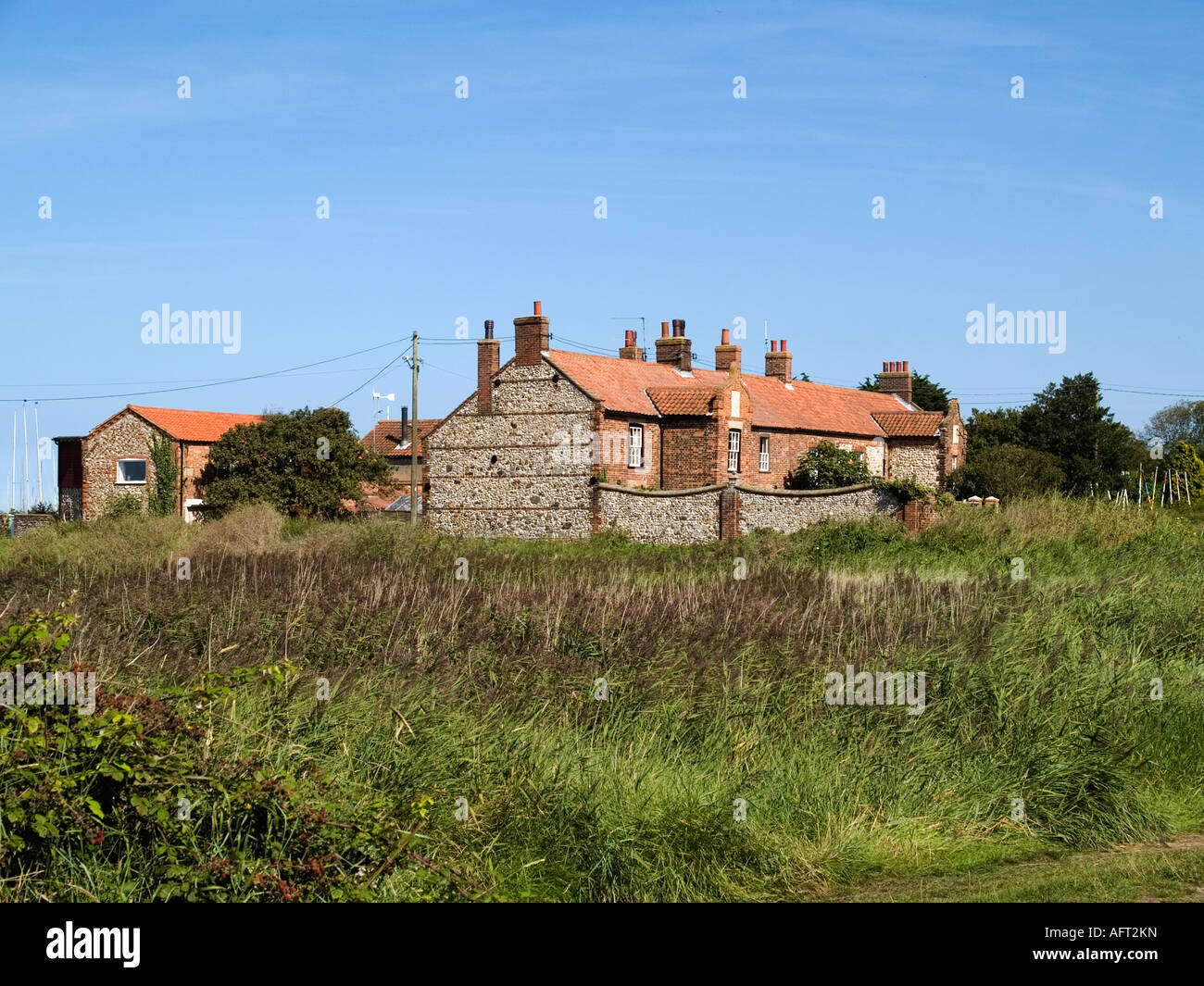Traditional flint walls and brick and tile cottages bordered by a reed