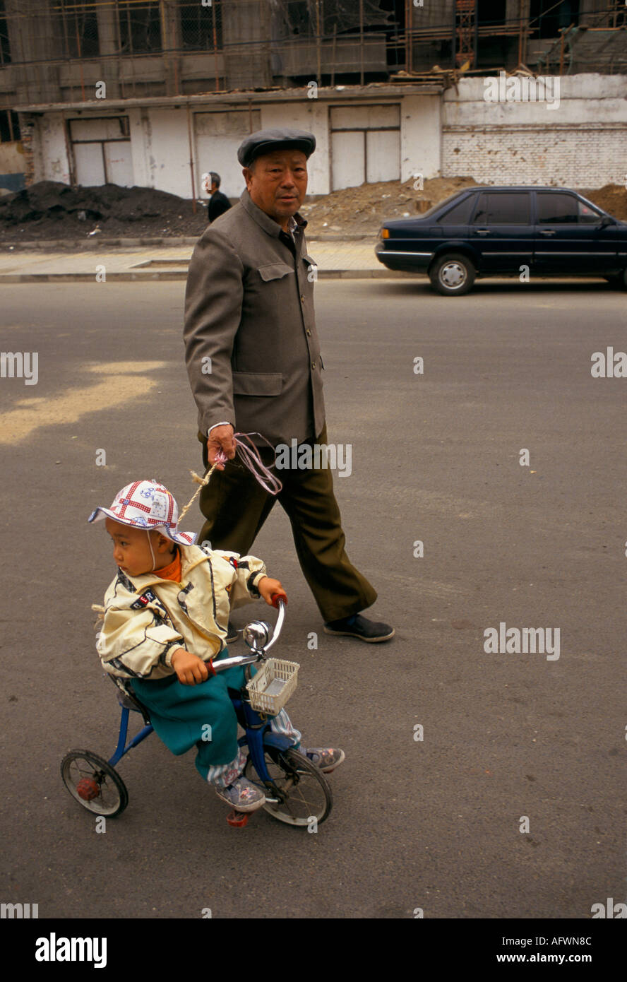 Beijing China 1998. Father and son daily life. Child in tricycle held on a rein by his dad. HOMER SYKES Stock Photo