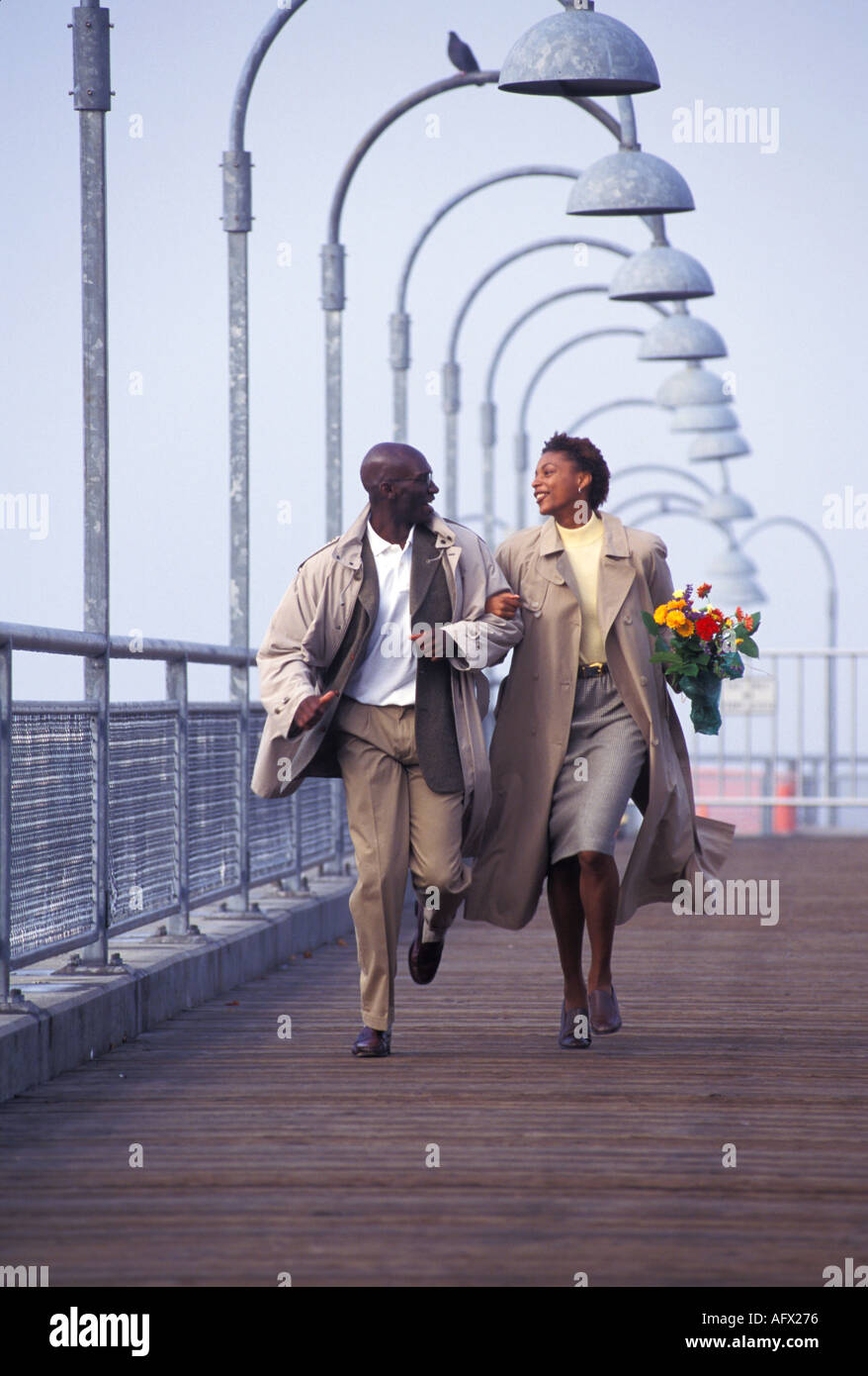 An African American couple run arm in arm on a dock Stock Photo