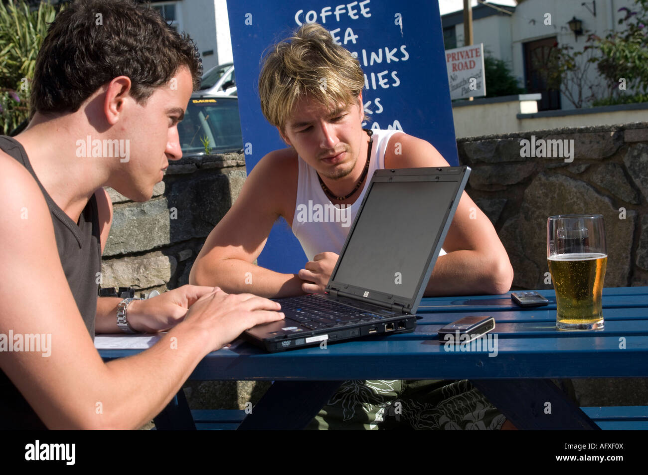 two young men using laptop wireless network outside The Vaynol pub Abersoch Gwynedd north wales while drinking lager beer Stock Photo