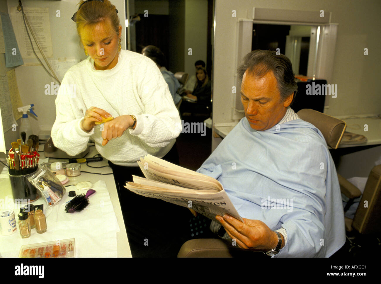 Peter Sissons British television news presenter being made up, makeup being applied before broadcast reading newspaper dressing room 1980s HOMER SYKES Stock Photo