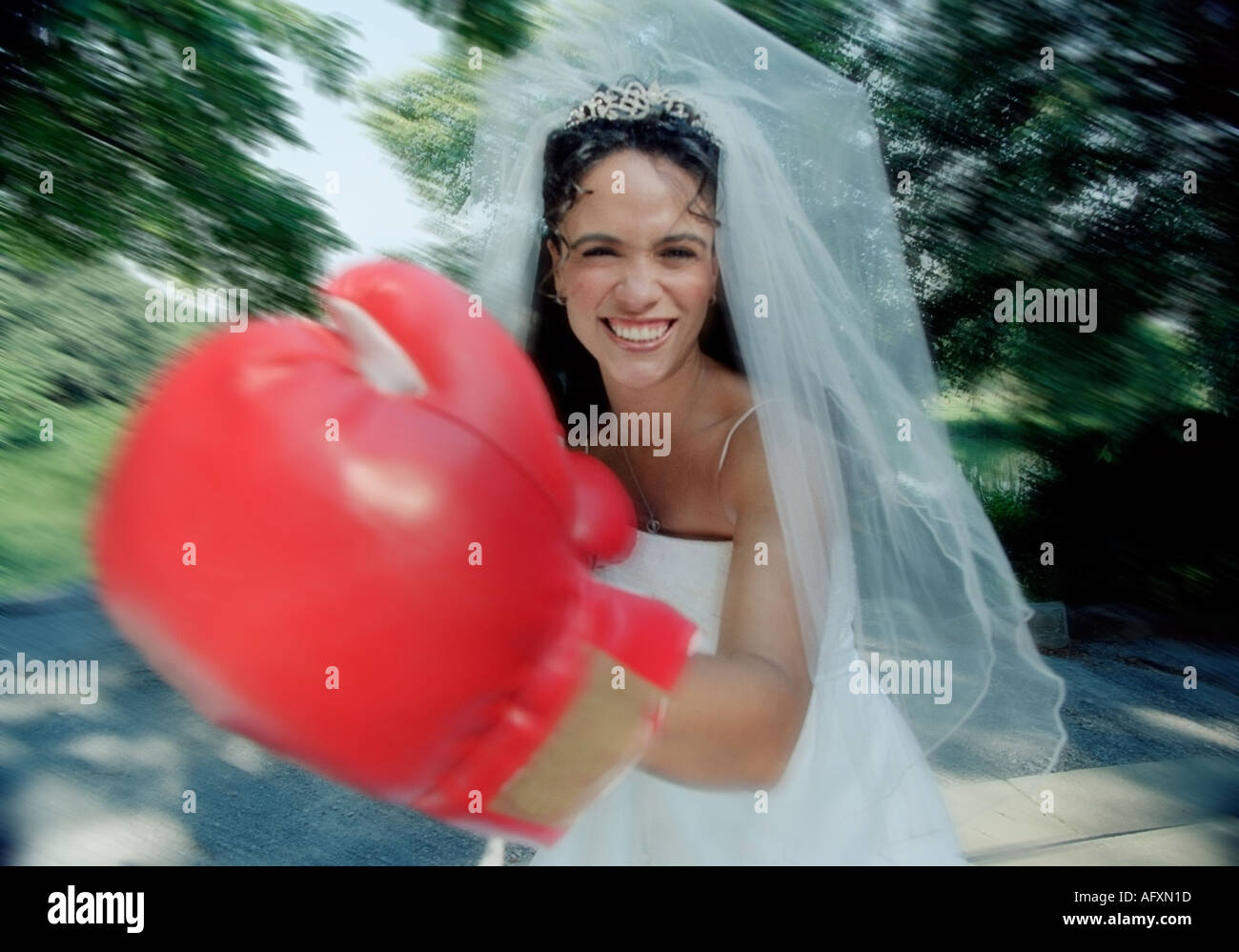 Bride play fighting in her wedding dress and veil wearing boxing gloves Stock Photo