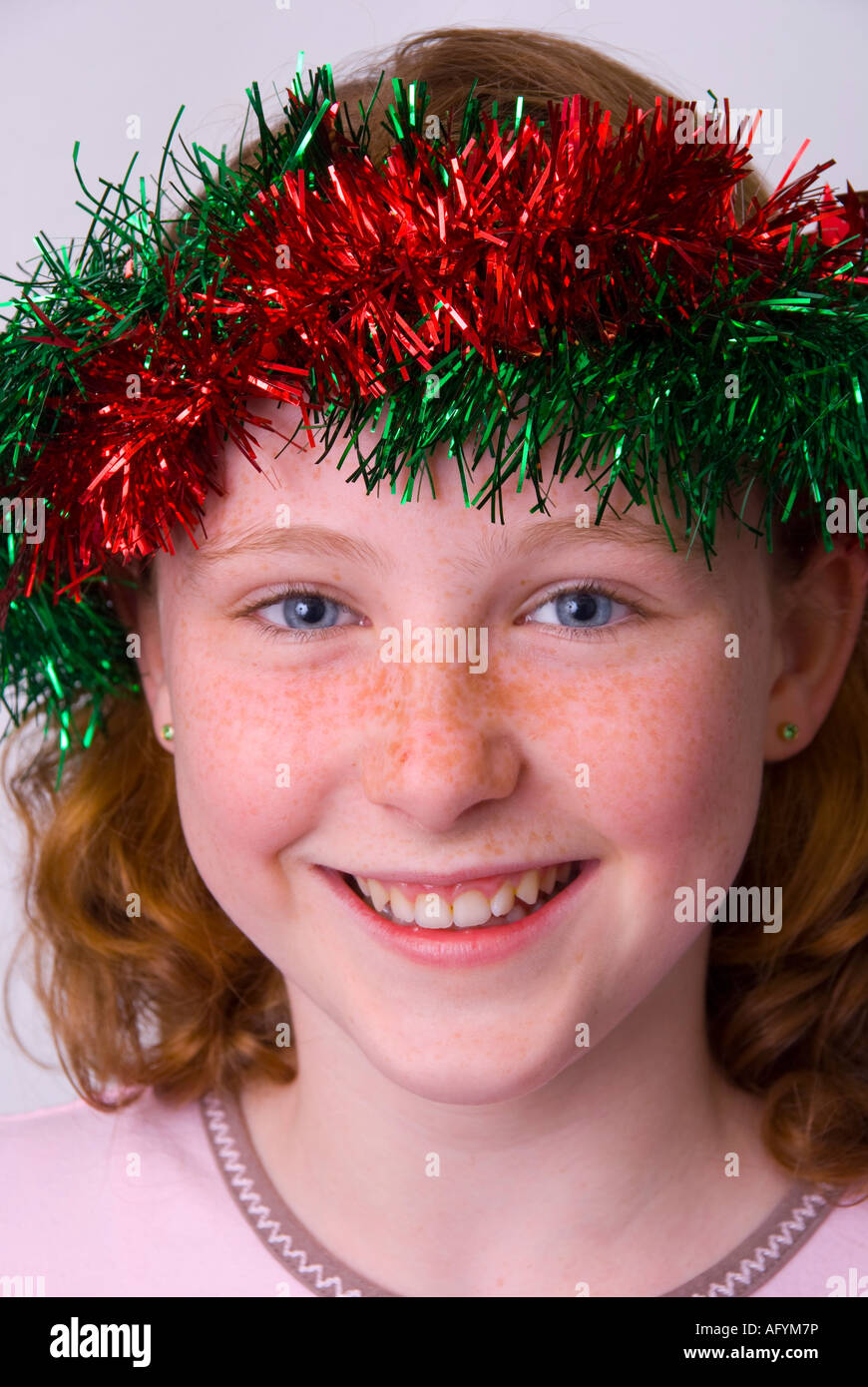 A smiling blue eyed freckle faced 11 year old girl of Irish origin wearing Christmas tinsel in her hair Stock Photo
