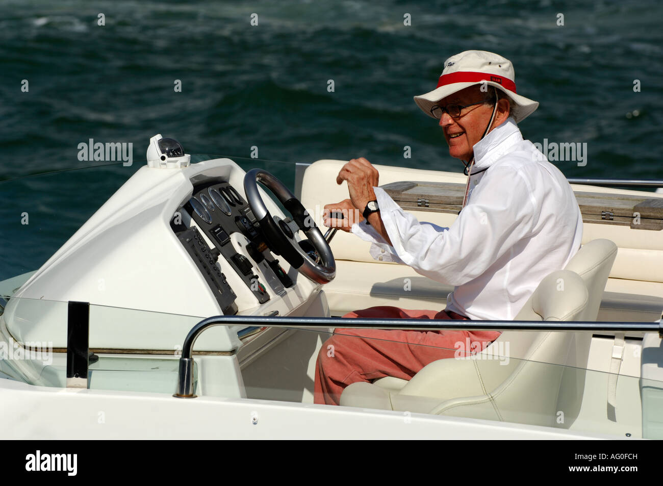 a middle aged gentleman at the helm of a luxury motor cruiser yacht at cowes on the isle of wight during cowes week Stock Photo