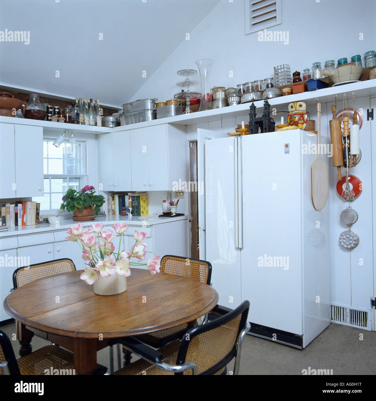 Circular wooden table and chrome & wi8cker chairs in white kitchen with large refrigerator Stock Photo