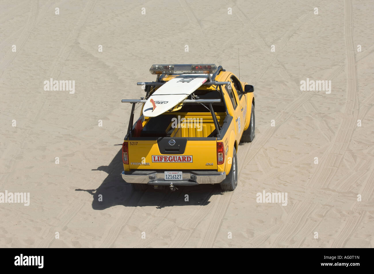 A lifeguard for Surf City USA, Huntington Beach patrols the oceanfront with a surfboard and yellow truck. Stock Photo