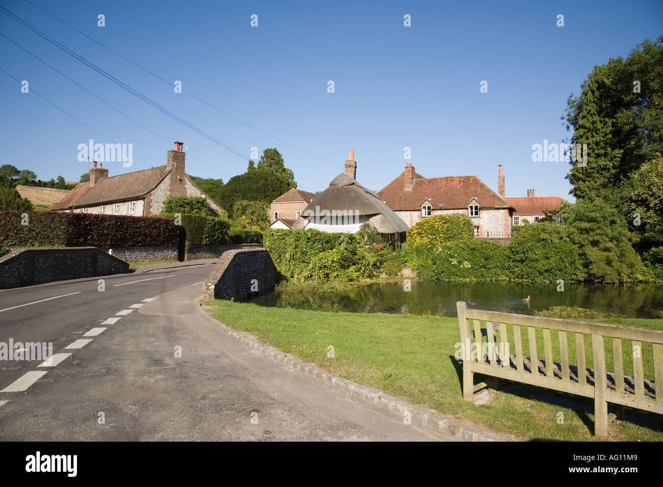Small road bridge and green by village pond with old cottages beyond in