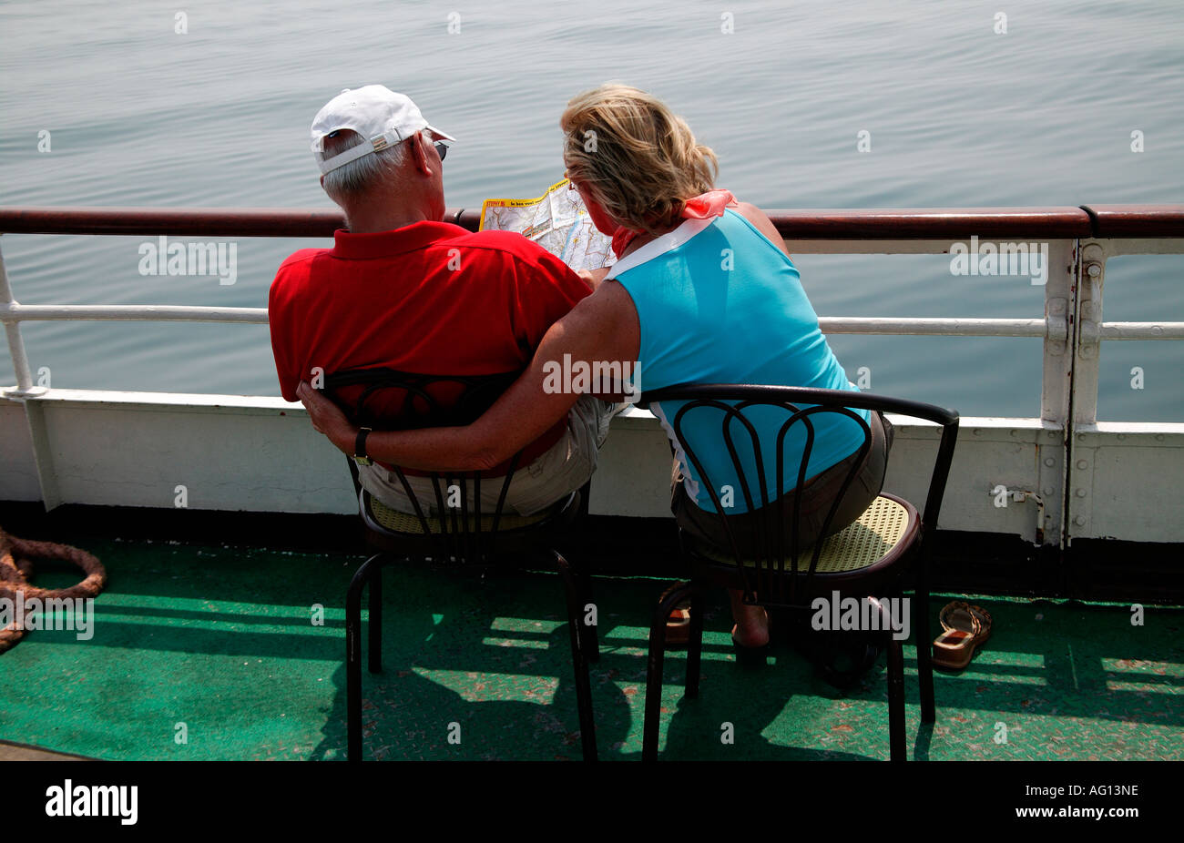 Older man and woman tourists on board a ferry, Lake Garda, Italy, with both looking at map of area Stock Photo