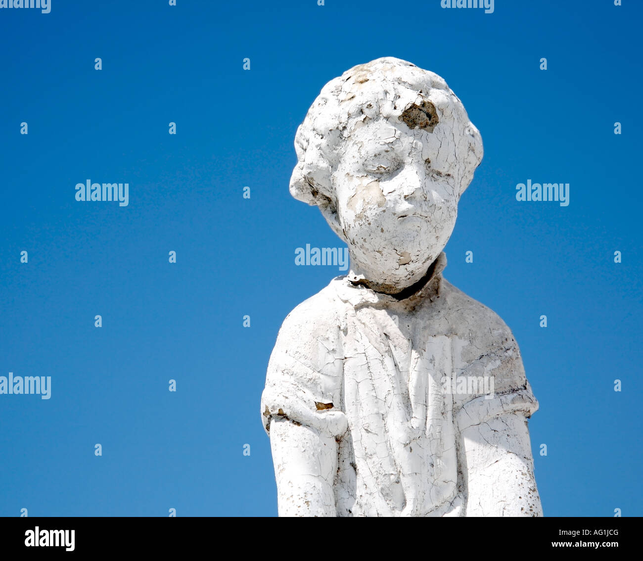 Close up of white stone boy statue in bad condition against a blue sky. Stock Photo