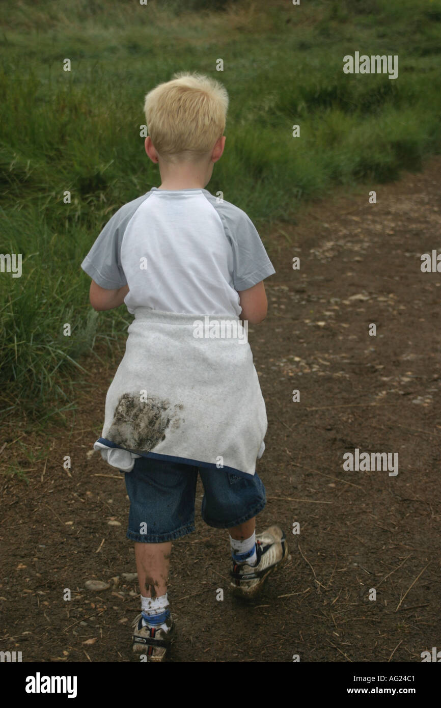 7 year old boy walking with muddy shoes and clothes Stock Photo